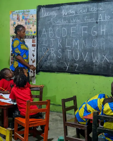 A teacher points at the alphabet on a blackboard while her class watches
