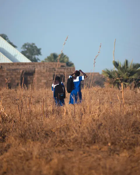 Pupils in uniform walking across a dry field towards school
